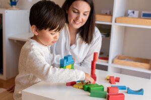 kid playing with wood blocks and teacher educador help